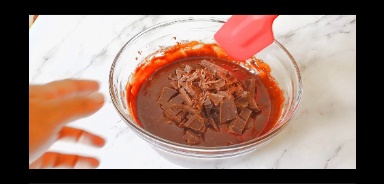 chopped chocolate is added to the bowl and folded using red rubber spatula