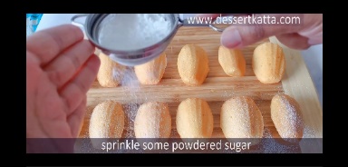 sprinkling powdered sugar on madeleines