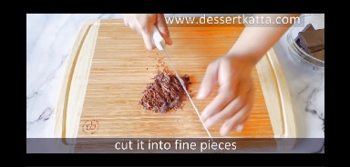 dark chocolate bar is cut using knife on wooden board