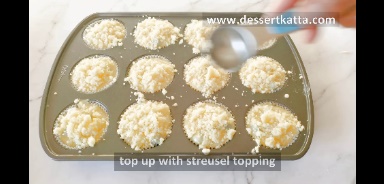 adding streusel topping to lemon blueberry muffins batter in muffins pan