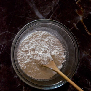 white powdered sugar in a bowl with wooden spoon placed on block marble background