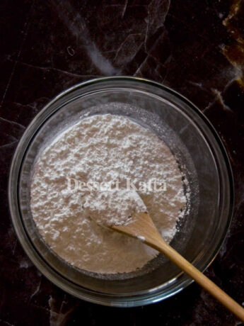white powdered sugar in a bowl with wooden spoon placed on block marble background