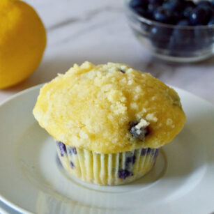 lemon blueberry muffins placed on small white plate with blueberries and lemon in background