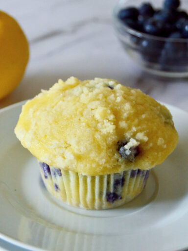 lemon blueberry muffins placed on small white plate with blueberries and lemon in background