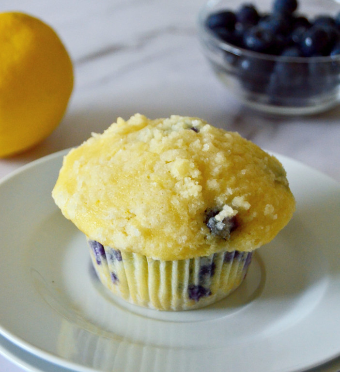 lemon blueberry muffins placed on small white plate with blueberries and lemon in background