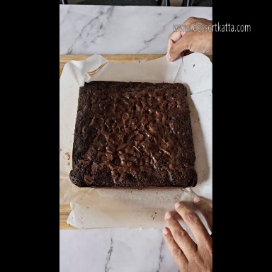 baked brownie slab is placed on parchment paper which is on wooden board