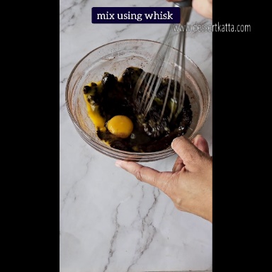 ingredients along with eggs are mixed in a big glass bowl using whisk