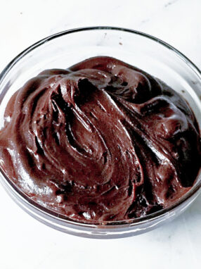 A glass bowl contains decadent chocolate brownie frosting