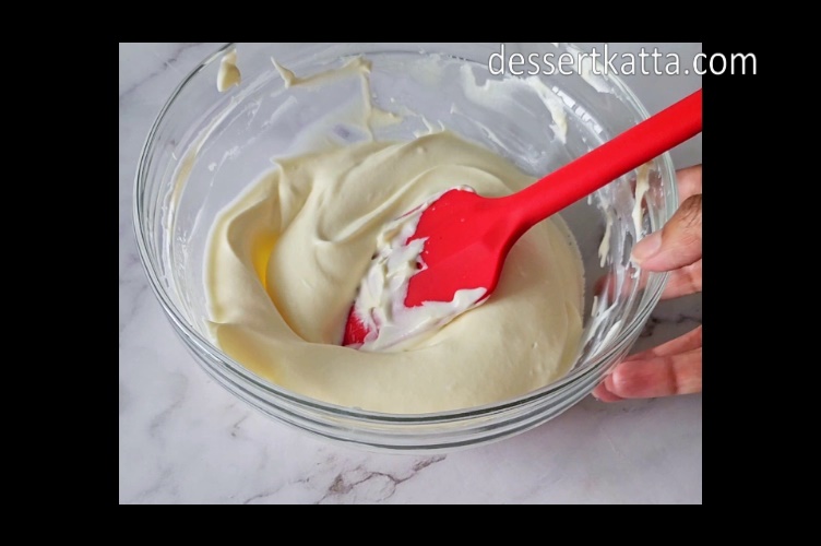 mixing bowl with vanilla pudding and whipped cream with red spatula kept on marble surface