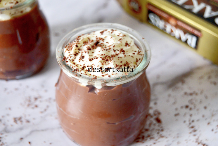 chocolate pudding topped with whipped cream and cocoa powder with packet of chocolate bar in back