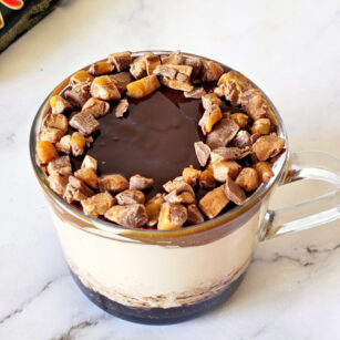 mars bar cheesecake topped with chocolate ganache and mars pieces in a mug