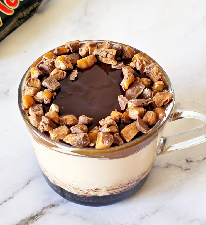 mars bar cheesecake topped with chocolate ganache and mars pieces in a mug