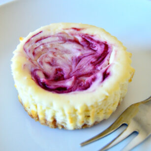 mini white chocolate and raspberry cheesecake is served on white plate with spoon