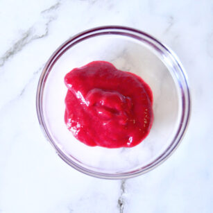 top view of raspberry sauce for cheesecake in a small bowl placed on marble surface