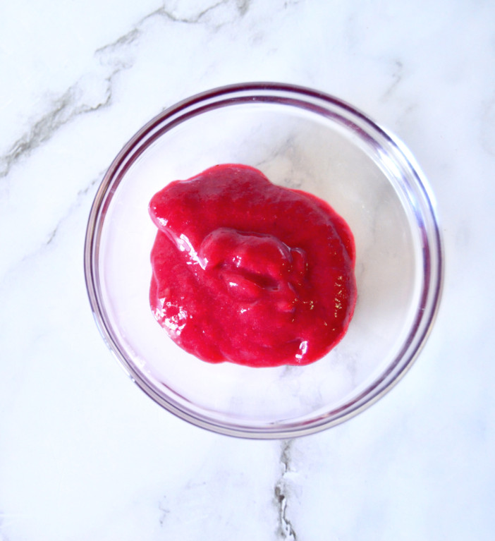 top view of raspberry sauce for cheesecake in a small bowl placed on marble surface