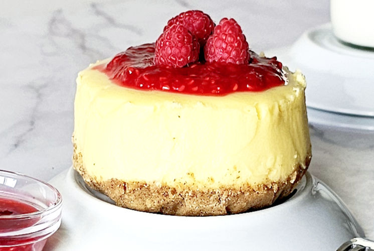 front shot of New York cheesecake with raspberry sauce and 3 raspberries on top