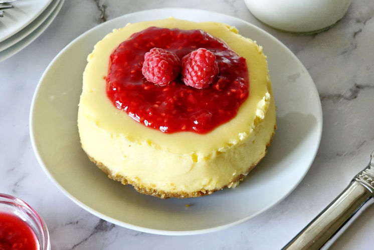 top shot of cheesecake topped with raspberries and raspberry sauce placed in serving plate