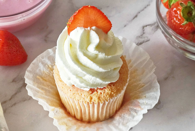 strawberry tres leches cupcake placed on marble surface with strawberry and strawberry milk in background